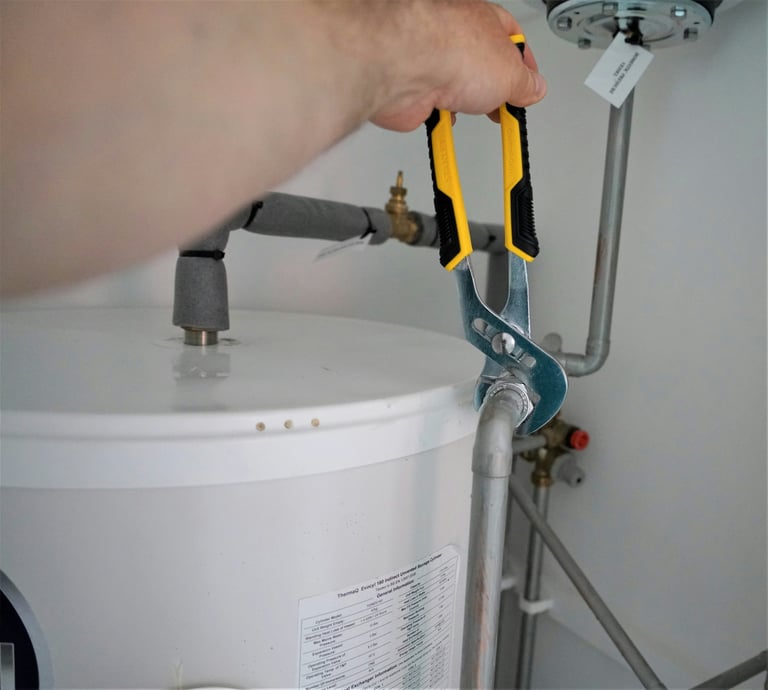 Person using pliers to adjust water heater valve connection with metal piping